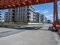 a large orange train is passing under a bridge over the water near some buildings with a city in the background