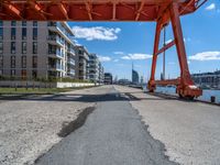 a large orange train is passing under a bridge over the water near some buildings with a city in the background