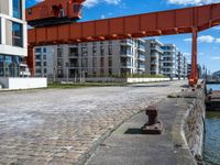 a large orange train is passing under a bridge over the water near some buildings with a city in the background