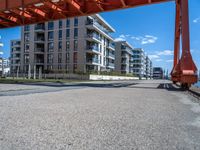 a large orange train is passing under a bridge over the water near some buildings with a city in the background