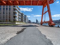 a large orange train is passing under a bridge over the water near some buildings with a city in the background