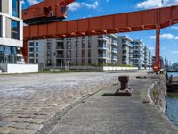 a large orange train is passing under a bridge over the water near some buildings with a city in the background