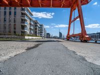 a large orange train is passing under a bridge over the water near some buildings with a city in the background