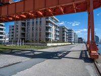 a large orange train is passing under a bridge over the water near some buildings with a city in the background