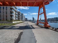 a large orange train is passing under a bridge over the water near some buildings with a city in the background