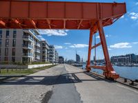 a large orange train is passing under a bridge over the water near some buildings with a city in the background