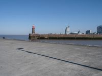 an open concrete road with a lighthouse in the distance and buildings by the sea side