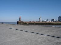 an open concrete road with a lighthouse in the distance and buildings by the sea side