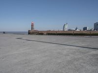 an open concrete road with a lighthouse in the distance and buildings by the sea side