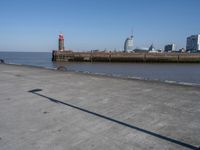 an open concrete road with a lighthouse in the distance and buildings by the sea side