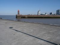 an open concrete road with a lighthouse in the distance and buildings by the sea side