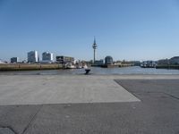 a cement paved road near water and a large cityscape on the horizon in the background