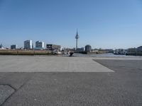 a cement paved road near water and a large cityscape on the horizon in the background