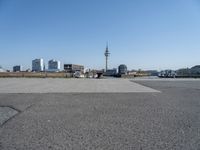 a cement paved road near water and a large cityscape on the horizon in the background