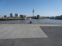 a cement paved road near water and a large cityscape on the horizon in the background