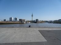 a cement paved road near water and a large cityscape on the horizon in the background