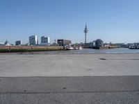 vehicles are parked by the street near the water and tall buildings on the other side