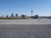 vehicles are parked by the street near the water and tall buildings on the other side