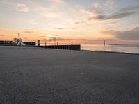 the sun is setting over the ocean and a dock is in the foreground with a beach in the distance