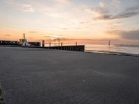 the sun is setting over the ocean and a dock is in the foreground with a beach in the distance