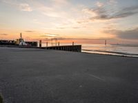 the sun is setting over the ocean and a dock is in the foreground with a beach in the distance