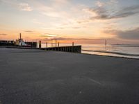 the sun is setting over the ocean and a dock is in the foreground with a beach in the distance