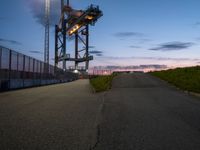 the tower is lit up as the sun sets on the horizon behind it, along with a path and grass, along which leads to an open, an empty highway