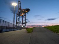 the tower is lit up as the sun sets on the horizon behind it, along with a path and grass, along which leads to an open, an empty highway