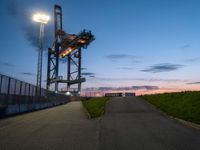 the tower is lit up as the sun sets on the horizon behind it, along with a path and grass, along which leads to an open, an empty highway