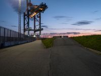 the tower is lit up as the sun sets on the horizon behind it, along with a path and grass, along which leads to an open, an empty highway