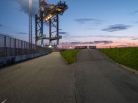 the tower is lit up as the sun sets on the horizon behind it, along with a path and grass, along which leads to an open, an empty highway