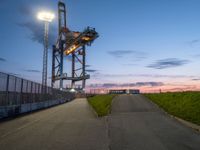 the tower is lit up as the sun sets on the horizon behind it, along with a path and grass, along which leads to an open, an empty highway