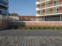 a sidewalk in front of a bricked area and large building in the distance with a fence on either side and to the right