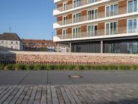 a sidewalk in front of a bricked area and large building in the distance with a fence on either side and to the right