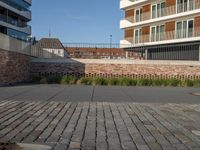 a sidewalk in front of a bricked area and large building in the distance with a fence on either side and to the right