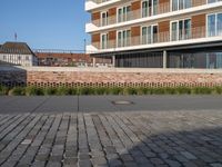 a sidewalk in front of a bricked area and large building in the distance with a fence on either side and to the right