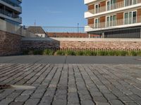 a sidewalk in front of a bricked area and large building in the distance with a fence on either side and to the right