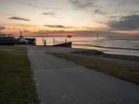 an empty path leads to the beach at sunset with a boat in the background and sun setting on horizon