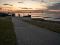 an empty path leads to the beach at sunset with a boat in the background and sun setting on horizon