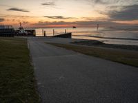 an empty path leads to the beach at sunset with a boat in the background and sun setting on horizon