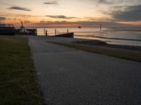 an empty path leads to the beach at sunset with a boat in the background and sun setting on horizon