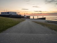 a long, paved road is near a grassy shoreline next to a pier in the evening