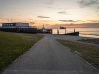 a long, paved road is near a grassy shoreline next to a pier in the evening