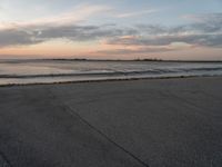 a person on a skate board skating in front of the ocean at sunset during a cloudy day