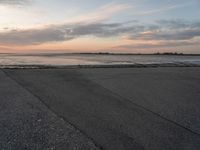 a person on a skate board skating in front of the ocean at sunset during a cloudy day