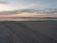 a person on a skate board skating in front of the ocean at sunset during a cloudy day