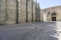 a stone area with a brick building and brick walkway in the background and light grey cobblestones