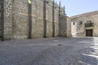 a stone area with a brick building and brick walkway in the background and light grey cobblestones