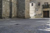 a stone area with a brick building and brick walkway in the background and light grey cobblestones