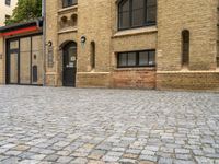 a brick paved street near an old building with windows and a door at the corner